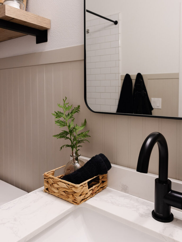 This photo shows a bathroom with beadboard, black accents and open shelving 